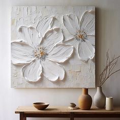 two white flowers are on the wall next to some vases and a wooden table