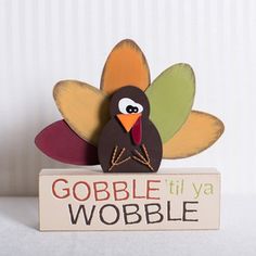 a wooden turkey sitting on top of a sign that says gobble til ya wobble