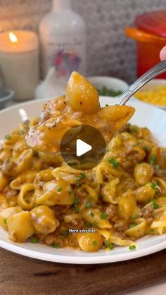 a person holding a spoon full of pasta with meat and cheese on it in a white bowl