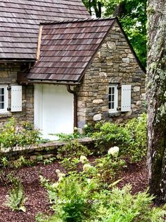 an old stone house in the woods with white doors and windows, surrounded by greenery