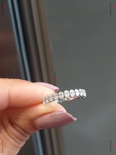 a woman's hand holding a diamond ring in front of a window with the reflection of another person