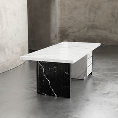 a white marble table sitting in front of a gray wall with black and white drawers