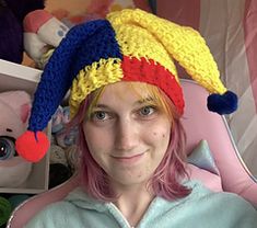 a woman with pink hair wearing a crocheted hat and smiling at the camera