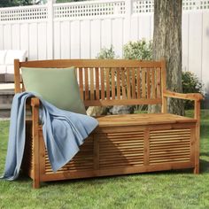 a wooden bench sitting in the grass next to a tree with a blanket on it