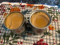 two tins filled with brown liquid sitting on top of a floral tablecloth covered place mat