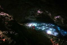 people are standing on the edge of a cave looking at blue and white lights in the water