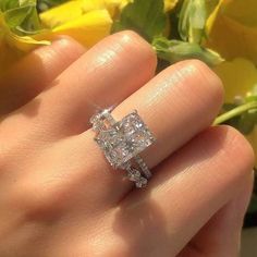 a woman's hand with a diamond ring on her finger and yellow flowers in the background