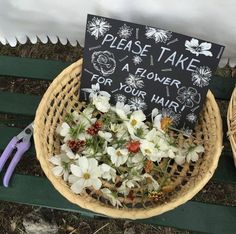 a basket filled with flowers sitting on top of a green bench next to a sign that says please take a flower for your hair