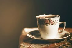 a tea cup and saucer sitting on top of a wooden table next to a wall