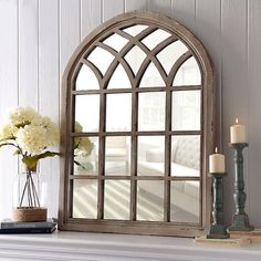 a white fireplace mantle with a mirror and flowers on it, next to a candle