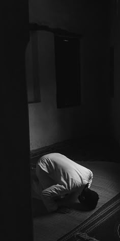 black and white photograph of a person laying on the floor in a dark room with his head down