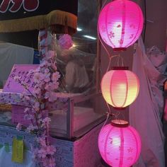 three pink lanterns hanging from the ceiling in front of a store display case with flowers on it