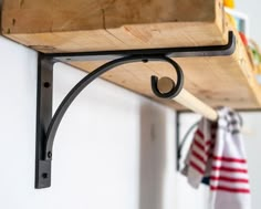 a wooden shelf with metal brackets and hooks hanging from it's sides on a wall