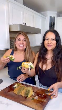 two women standing in front of a cutting board with food on it