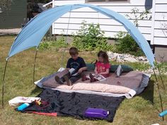 two children are sitting on a blanket in the grass reading books under an umbrella tent