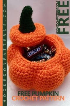 an orange crocheted pumpkin with a black hat on it's head and candy bar in its mouth