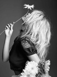 a black and white photo of a woman with flowers in her hair blowing the wind