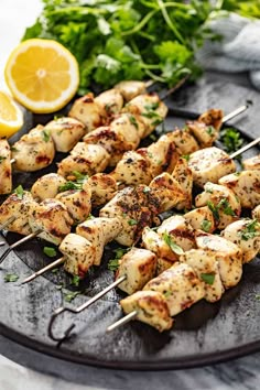 chicken skewers with lemon wedges and parsley on a black platter