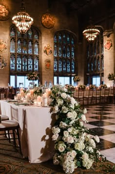 a table with white flowers and candles on it in front of large chandeliers