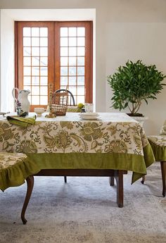 a dining room table covered with a green and white blanket next to two chairs in front of a potted plant