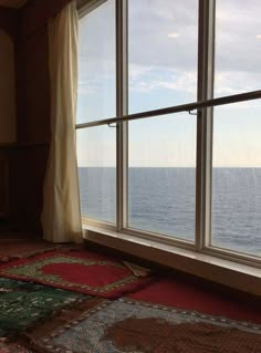 a large open window overlooking the ocean with rugs on the floor in front of it