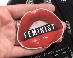 a person holding a sticker with the word feminist on it in front of their mouth