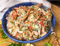 a blue bowl filled with shrimp, carrots and parsley sprinkled slaw