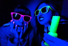 two girls wearing neon glasses and one is holding a fluorescent colored object in her hand