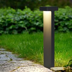 a light that is sitting on the side of a road near some grass and bushes