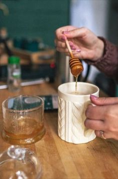 a person pouring honey into a cup on top of a wooden table