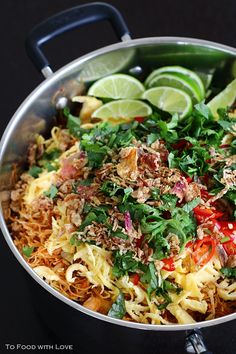 a pan filled with noodles and vegetables on top of a table next to lime wedges