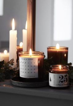 three candles are sitting on a table with greenery around them and the number twenty five is placed next to it