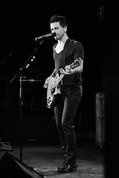 a man standing in front of a microphone while holding a guitar