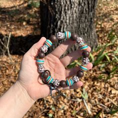 a person holding onto a bracelet with beads and charms on it in front of a tree