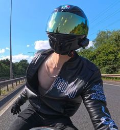 a woman wearing a leather jacket and helmet riding a motorcycle down the road on a sunny day