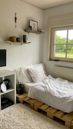 a bed with white sheets and pillows in a small room next to a large window