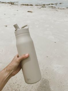 a hand holding a gray water bottle on the beach