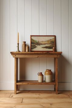 a wooden table with two vases and a painting on the wall next to it