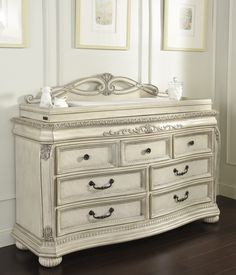 a white dresser with drawers and pictures on the wall