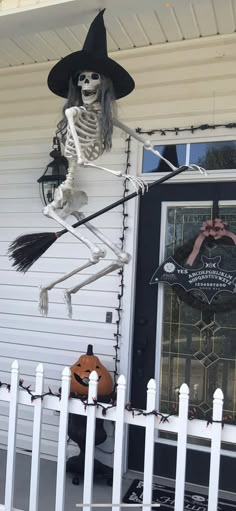 a skeleton in a witches hat is hanging on the front door of a house with a broom