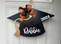 a black graduation cap hanging on the front door with orange ribbon and name written on it