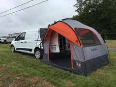 an orange and gray tent sitting in the grass next to a van with its door open