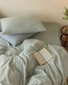 an open book sitting on top of a bed next to two pillows and a lamp