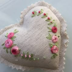 a heart shaped pillow with pink flowers on the front and side, sitting on top of a table