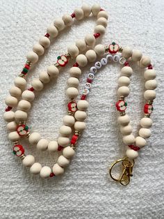 a white beaded necklace with red and green beads, gold clasps and a charm