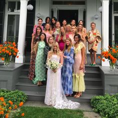 a group of women standing on the front steps of a white house with orange flowers