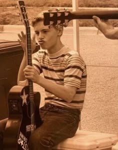 a young man sitting on top of a toilet next to a guitar