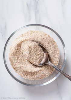 a glass bowl filled with brown and white powder next to a spoon on top of a marble counter