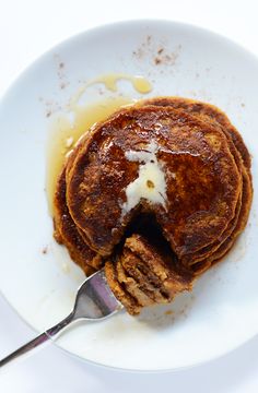 a white plate topped with pancakes covered in butter and syrup next to a fork on top of it