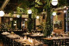 an indoor dining area with tables and chairs covered in greenery, surrounded by hanging lights